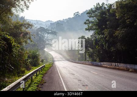 Misty morning in Nam Nao National Park, Thailand. A foggy road winds through lush forest. Tropical jungle surrounds the scenic highway. Stock Photo