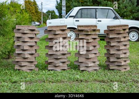 Four stacks of interlocking paving stones on grass, near a white car Stock Photo