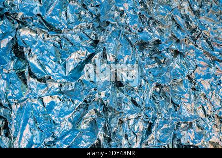 Shiny crumpled blue metallic foil reflecting light creating an abstract texture background Stock Photo