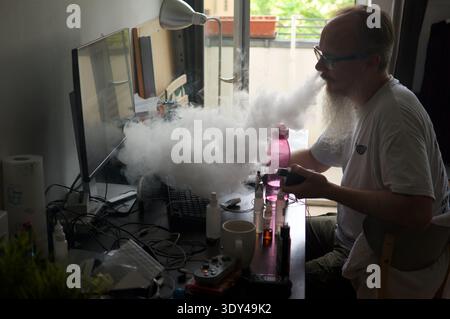 Bearded man smoking a vape in a cloud of smoke whilst watching television Stock Photo