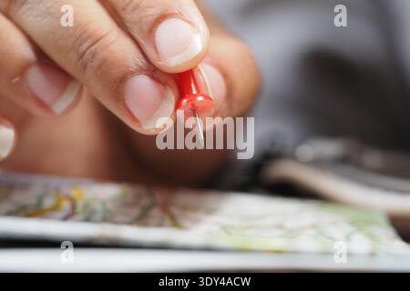 Holding a red push pin above a map on the table Stock Photo