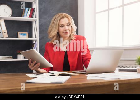 Happy businesswoman working on laptop and holding digital tablet Stock Photo
