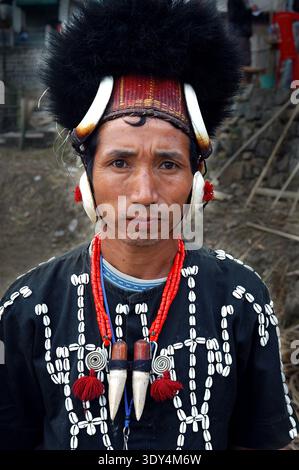 A naga man with their traditional dress. Nagaland, a state in northeastern India, is home to a diverse population of tribal groups, each with its own unique culture and traditions. The majority of the people belong to various tribes and sub-tribes, such as the Ao, Konyak, Sumi, and Angami, among others. These communities primarily live in rural areas, where they continue to engage in traditional activities like farming and weaving, which are central to their livelihood. Agriculture, particularly rice cultivation, plays a crucial role in their economy. India. Stock Photo