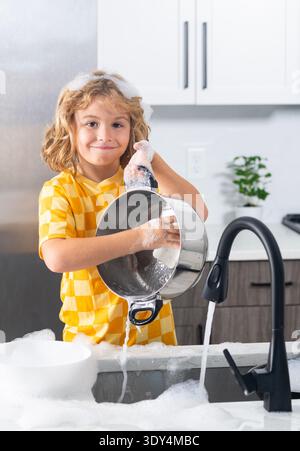 Child playing with foam in kitchen. Cute kid cleaning dishes at home. Happy child splashing soap foam. Funny boy enjoying house chores. Child having Stock Photo