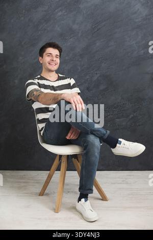Young smiling man sitting at gray studio background Stock Photo