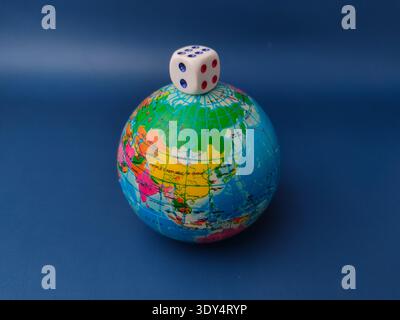 A white dice showing the numbers four and six is placed on top of a miniature globe. Stock Photo