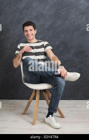 Young smiling man sitting at gray studio background Stock Photo