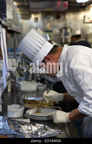 Chef plating a dish with sauce in kitchen Stock Photo