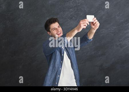 Young man taking selfie on smartphone at gray background Stock Photo