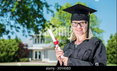 Middle aged woman with diploma in hand. Wearing a graduate uniform Stock Photo