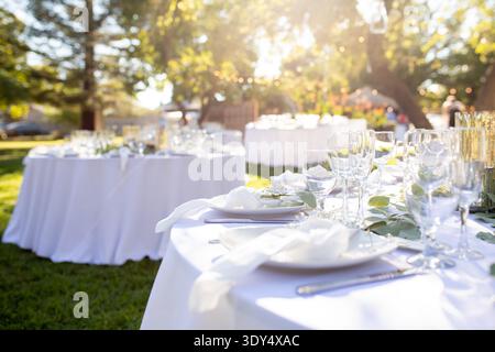 Outdoor wedding reception table set with glassware, candles and greenery centerpiece arranged for celebration dinner. Stock Photo