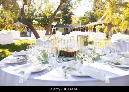 Outdoor wedding reception table set with glassware, candles and greenery centerpiece arranged for celebration dinner. Stock Photo