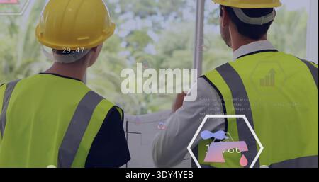 Examining two engineers studying plans at window, wearing yellow hard hats, neon vests with HUD Stock Photo