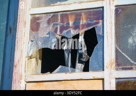 Damaged window with torn plastic sheet and taped cracks. Urban decay, abandonment, renovation need and architectural deterioration concept Stock Photo