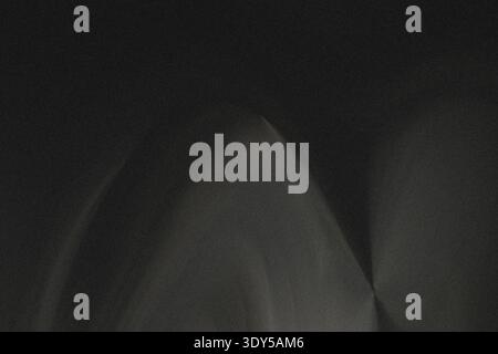 A blurry dark photograph showing a faint white light source illuminating a dark gray background space area Stock Photo