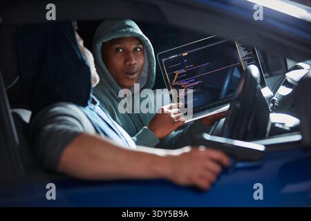 Criminal, hackers or laptop screen with code in car for ransomware, phishing or stealing data. Theft, tech display or men with cybercrime in vehicle Stock Photo