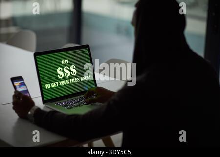 Hacker, person or laptop screen with phone in office for ransomware, data theft or payment demand. Extortion, tech or criminal with cybercrime at Stock Photo
