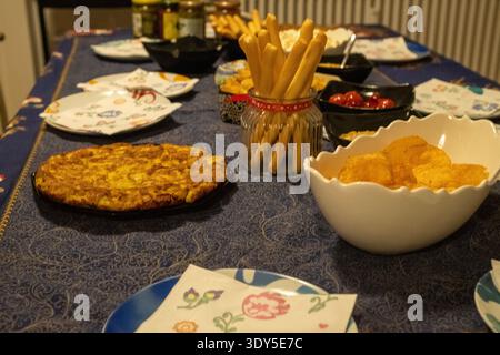 Dining table set with a blue tablecloth, on the table there are various appetizers such as tortillas, chips and breadsticks Stock Photo