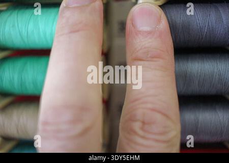A man's hand touching rows of vibrant, multi-colored spools of thread. High-quality detail focusing on texture and the variety of textile materials fo Stock Photo
