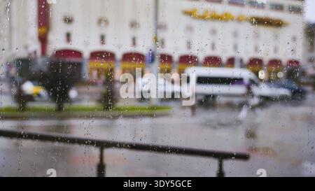 Raindrops on glass seeing out of focus city street with cars and buildings on a wet day Stock Photo