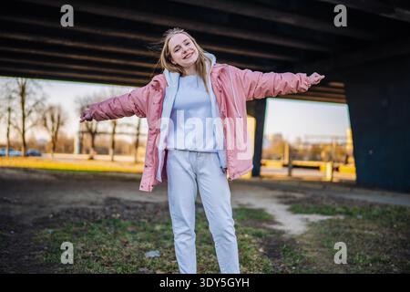 Young woman enjoying freedom, smiling with arms wide open in urban setting Stock Photo