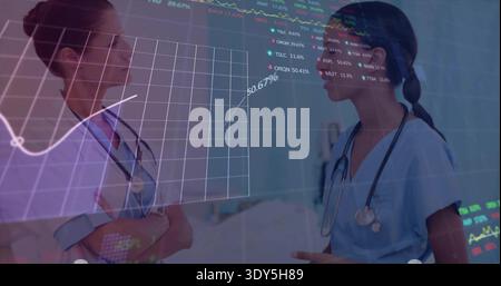 Discussing two nurses reviewing data in ward corridor with stethoscopes, blue scrubs, bed 50 Stock Photo