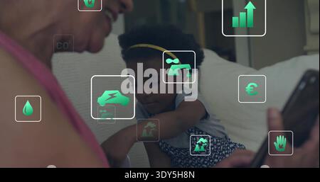 Smiling senior woman in pink top, child reaching toward phone on sofa at home, green icons Stock Photo