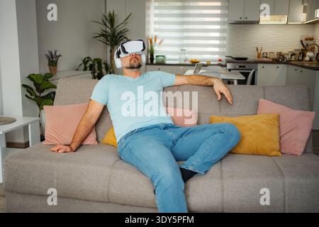 Man wearing VR headset relaxing on sofa at home Stock Photo