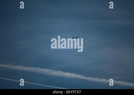 Airplane flying across a clear blue sky, leaving white contrails behind it Stock Photo