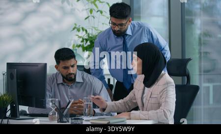 Arabian Muslim business team three colleagues arguing in office Islamic Indian woman in hijab and two businessmen discussing work data pointing on Stock Photo