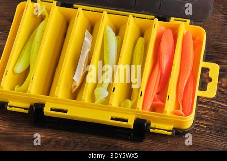 Yellow plastic fishing tackle box open, organized with various colorful soft plastic fishing lures in separate compartments Stock Photo