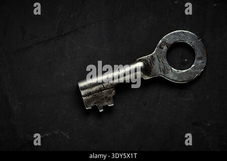 Close up an antique metal key on dark textured background, metaphor for accessing secrets Stock Photo
