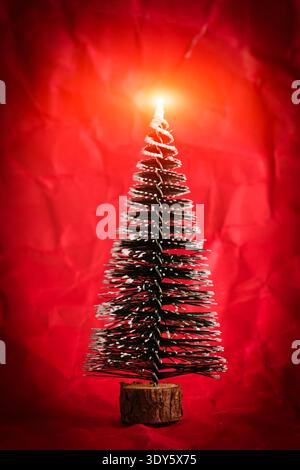 Small snowy Christmas tree with bright glowing star on top on red background. Holiday concept Stock Photo