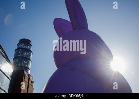 Giant inflatable violet Easter bunny statue standing outside in city downtown in sunny spring day close up. Traditional Easter celebration city decora Stock Photo