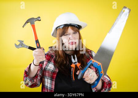 Woman struggling with various construction tools on yellow background Stock Photo