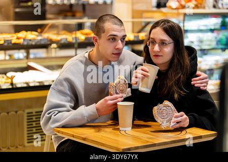 A young woman and a man are drinking coffee with buns in a cafe. Stock Photo