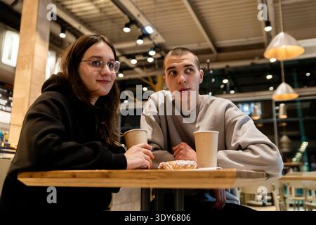 Young couple enjoying cinnamon rolls and coffee together at cafe Stock Photo