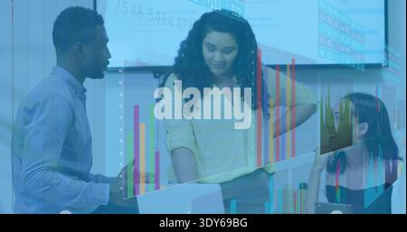 Reviewing team of three in business casual analyzing charts at meeting table with laptop and files Stock Photo