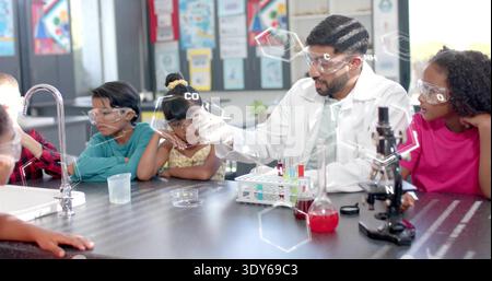 Male science teacher lifting flask and showing reaction in lab, hexagons aligning with teacher hand Stock Photo