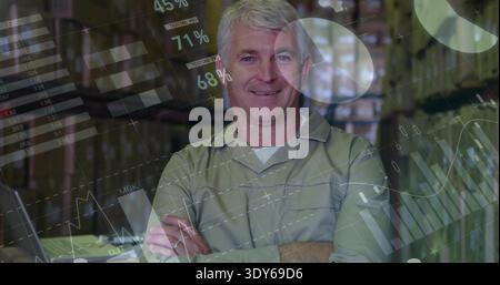 Standing supervisor wearing work shirt, crossing arms in aisle of tall racks with laptop and charts Stock Photo