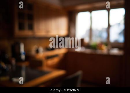 Out of focus shot of a warm wooden kitchen with bright natural light coming through a large window, creating a cozy domestic atmosphere, wide angle, n Stock Photo