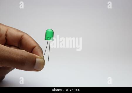 Green light emitting diode or LED held in the hand by its connecting pin on the white background Stock Photo