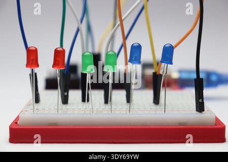 Light emitting diodes of red, green and blue color on a breadboard connected by jumper cables and controlled by a microcontroller on background Stock Photo