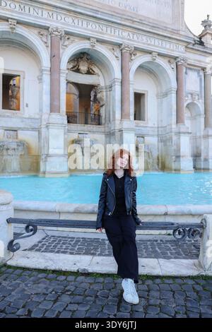 Young woman sitting by a historic fountain with classical architecture. Travel and tourism concept in a European city. Stock Photo