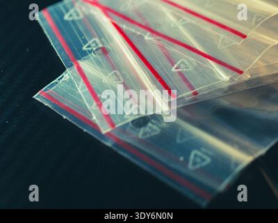 Clear plastic bags with red seals lie stacked. Bright stripes contrast against dark background. Each bag holds a subtle triangular icon. Ideal for ret Stock Photo
