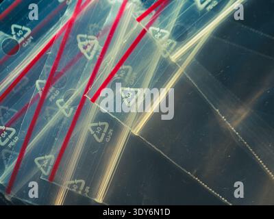Clear plastic bags with red zippers lie stacked. Each bag bears a recycling symbol in white. Light reflects off their glossy surfaces. They appear unu Stock Photo