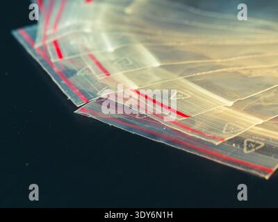 Clear plastic bags with red sealing edges lie stacked. Soft light glints across their smooth, transparent surfaces. Dark background contrasts the bags Stock Photo