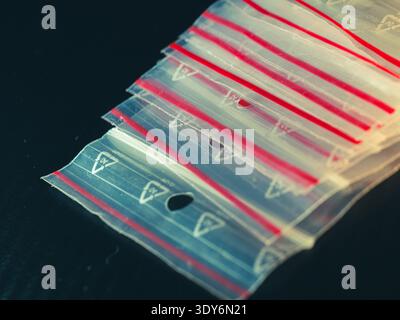 Stack of clear plastic bags with red seals and triangular cutouts. Bags lie on dark surface, neatly arranged. Red lines highlight bag edges, creating Stock Photo