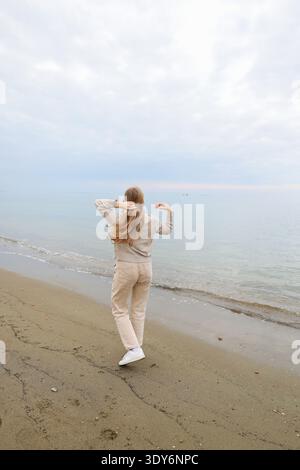 Happy young woman standing on a sandy beach with open arms by the sea. Freedom and travel concept. Stock Photo