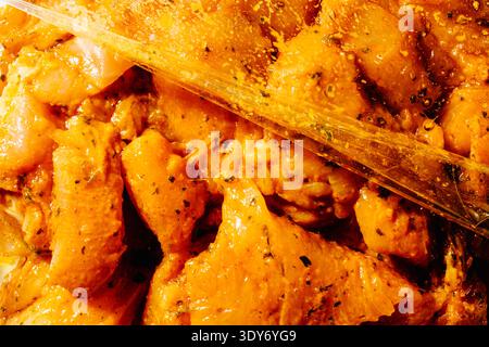 closeup of seasoned raw chicken pieces marinating inside a transparent plastic bag, covered with spices and oil, preparation of meat before cooking in Stock Photo